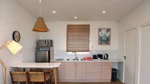 A compact kitchen with a white countertop, stainless steel appliances, and a wooden dining table with wicker chairs. - A modern, well-equipped bungalow with an exceptional view of the lagoon! (Bora-Bora)