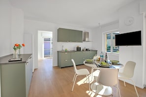 Una cocina moderna con armarios verdes, una zona de comedor con sillas blancas y un televisor montado en la pared.