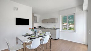 A modern kitchen with white cabinets, a flat-screen TV, and a dining area with white chairs and a table set for two. - Ulivo and Magnolia Bike & River Apartment (Arco)