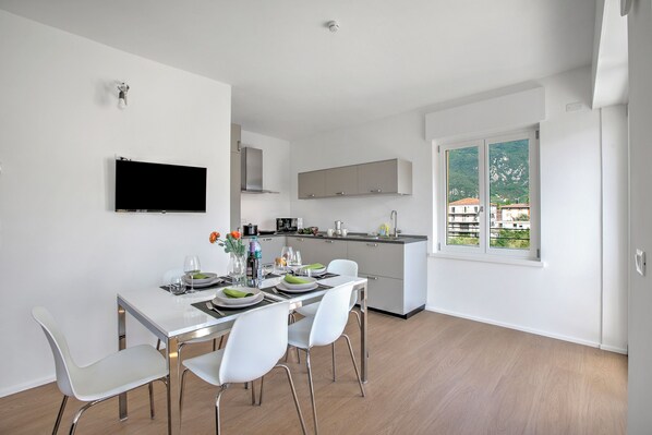 Une cuisine moderne avec des meubles blancs, un téléviseur à écran plat et un coin repas comprenant des chaises blanches et une table dressée pour deux personnes.