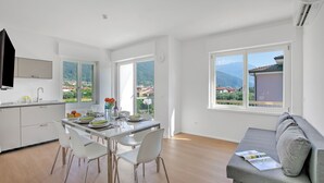 A modern kitchen with white cabinets, a dining table with chairs, and large windows offering a view of a mountainous landscape. - Ulivo and Magnolia Bike & River Apartment (Arco)