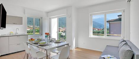 A modern kitchen with white cabinets, a dining table with chairs, and large windows offering a view of a mountainous landscape.