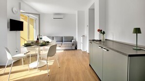 A modern kitchen with a dining area, a sofa, and a TV mounted on the wall. - Ulivo and Magnolia Bike & River Apartment (Arco)