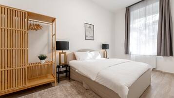 Um quarto moderno com uma cama grande, um guarda-roupa de madeira, duas mesas de cabeceira com abajures, um quadro na parede e uma janela com cortinas.