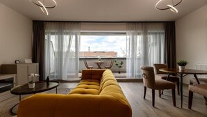 Una sala de estar moderna con sofá, una mesa de comedor, sillas y vista a un edificio a través de amplios ventanales.