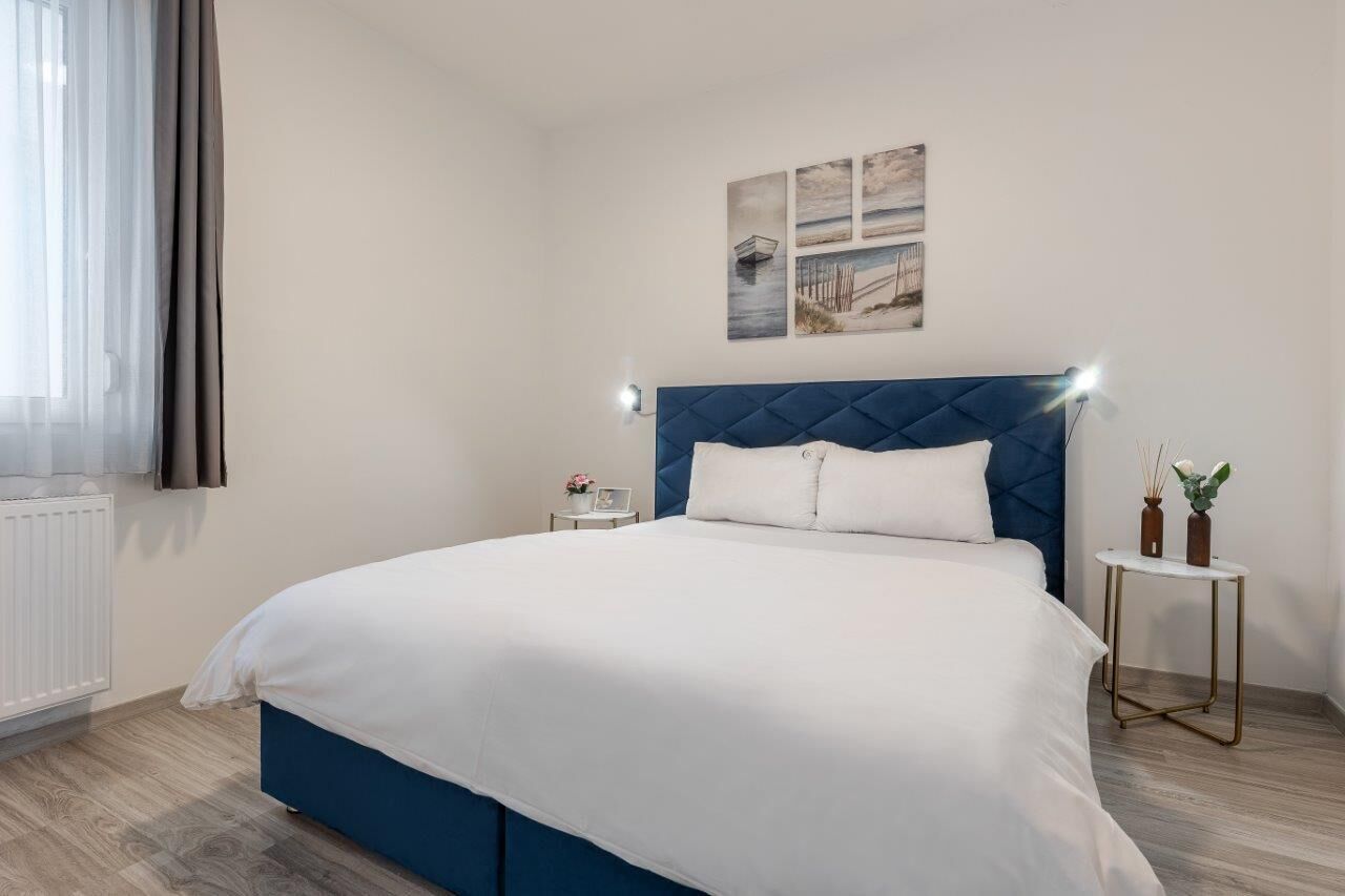 A neatly arranged bedroom with a large bed, a bedside table with a lamp, and a small table with decorative items.