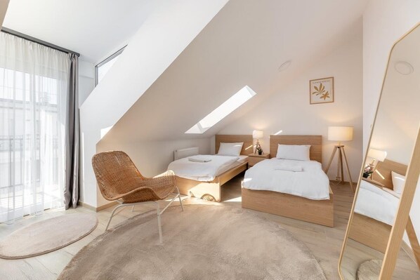A modern hotel room with a sloped ceiling, two beds, a large mirror, and a view of the city. - Magnolia Apartment Hotel (Budapest)