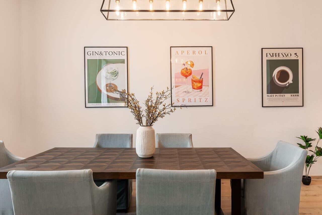A dining area with a wooden table and four chairs, a vase with branches, and three posters on the wall.