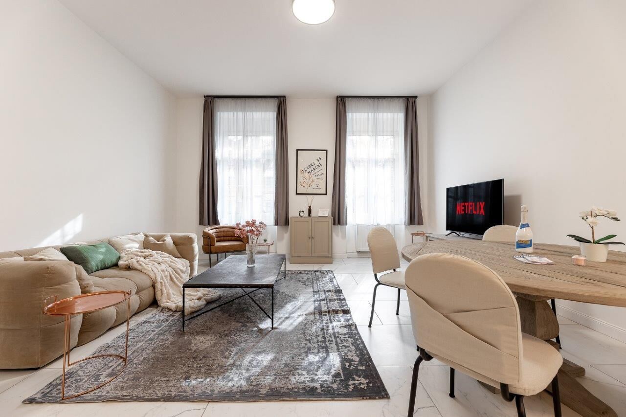 A modern living room with a sofa, coffee table, dining table, and chairs. There is a TV and a cabinet in the room.