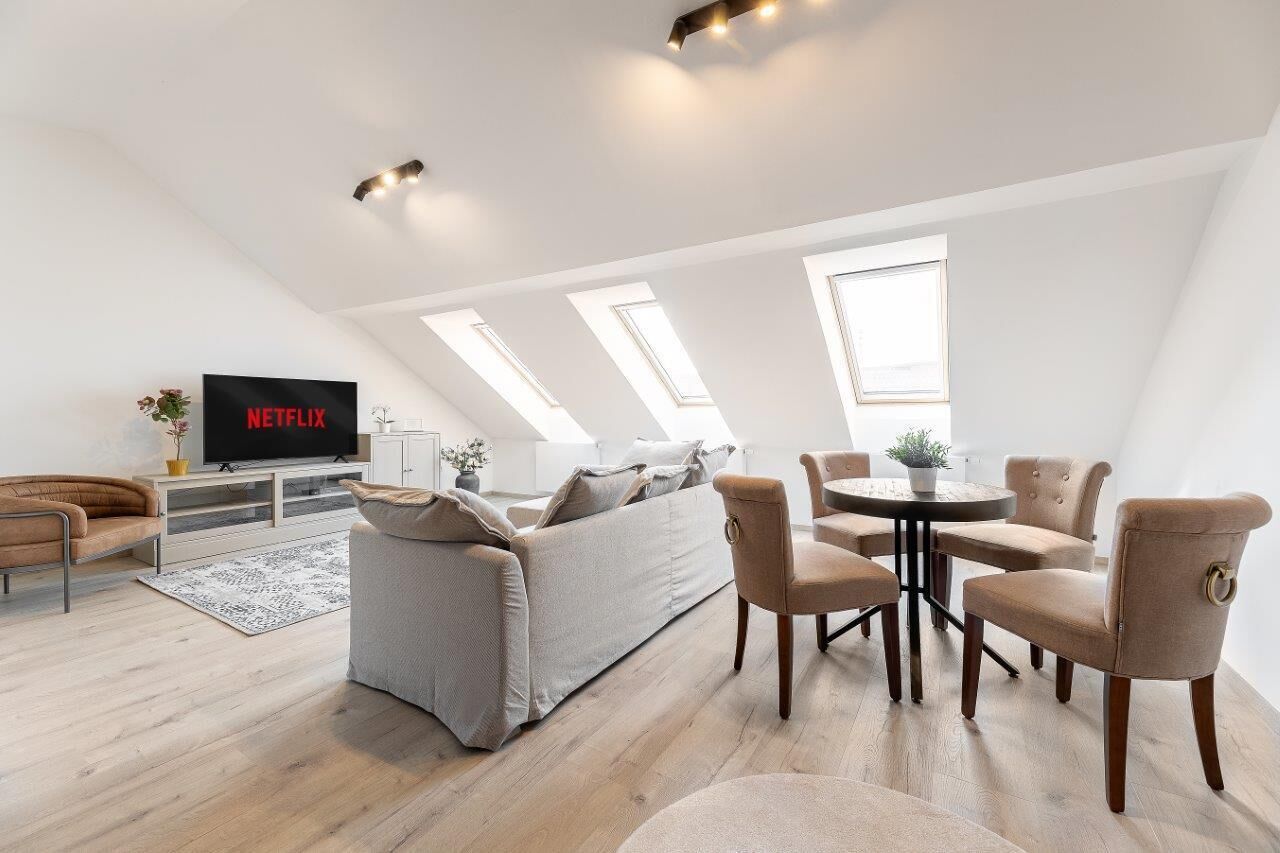 A modern loft apartment with a large sofa, a dining table, and a TV displaying 'NETFLIX'.