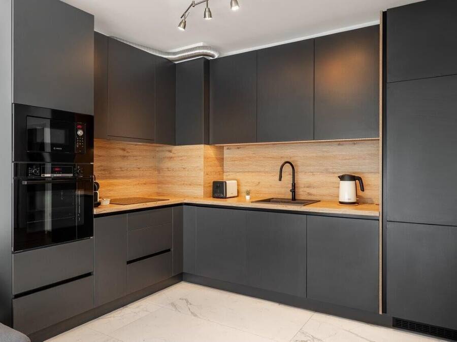 Een moderne keuken met donkere kasten, een houten spatwand, een inbouwoven, een magnetron, een broodrooster en een waterkoker.