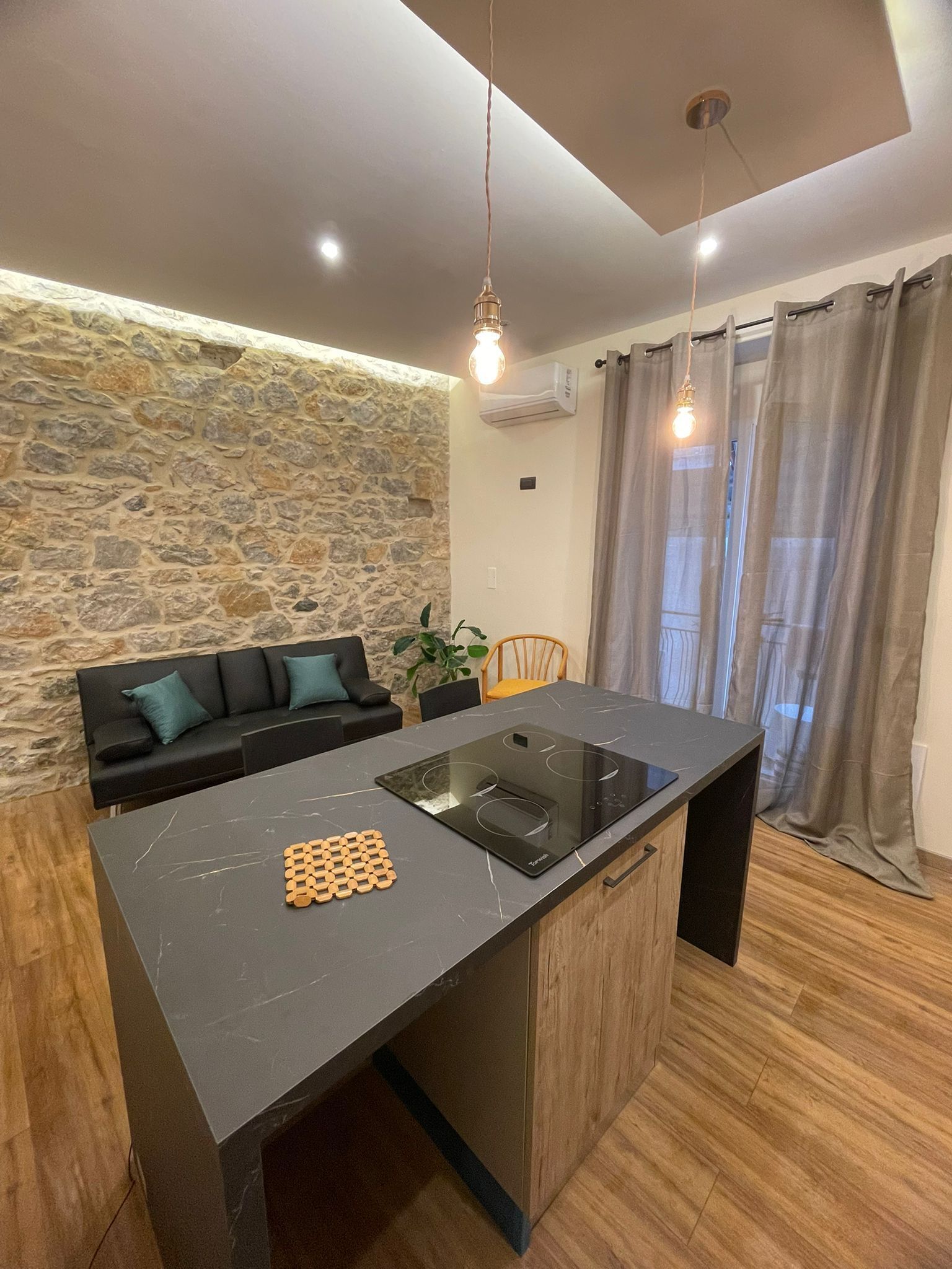 Uma cozinha moderna com ilha central, parede de pedra e um espaço de estar aconchegante com sofá e cadeiras.
