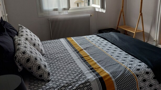 Un dormitorio con cama, ventana con cortinas, radiador y un perchero de madera.