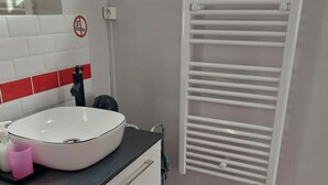 Un baño con un lavamanos blanco, un espejo, un perchero para toallas y un pequeño taburete.