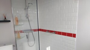 Un baño moderno con ducha de vidrio, paredes de azulejos blancos y un detalle en color rojo.