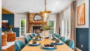 A dining room with a long table set for six, a fireplace, and a stone wall.