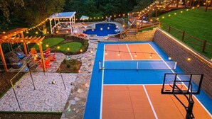 A backyard with a basketball court, a pool, and a covered seating area.