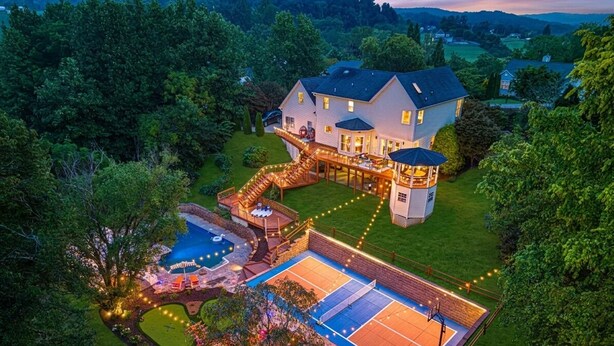 A large house with a tennis court, a swimming pool, and a covered patio area.