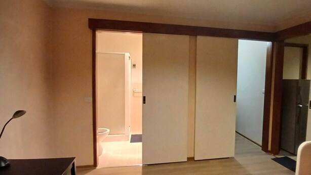 Ein Hotelzimmer mit einer Schiebetür zu einem Badezimmer, einem Schreibtisch mit Lampe und einem Bett mit Kopfteil.