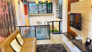 A modern living room with a brown leather sofa, a black circular rug, a glass railing, a TV mounted on the wall, and a kitchen area with a window. - Quattrick Villa (Batu Sub-District)