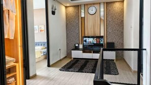 A modern living room with a flat-screen TV, wooden panel wall, and a clock. - Quattrick Villa (Batu Sub-District)