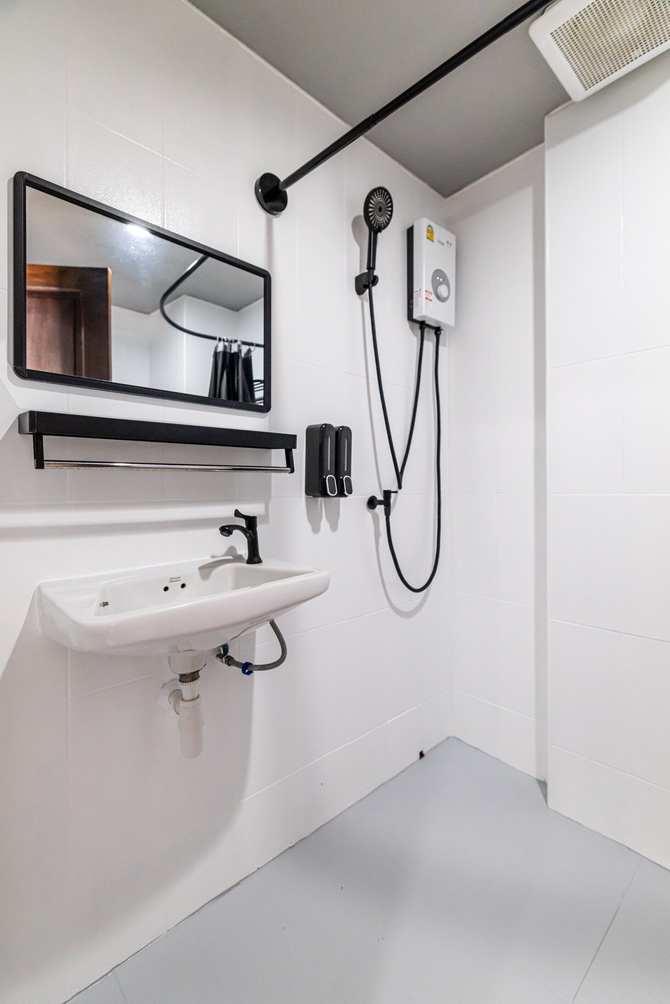 A modern bathroom with a white sink, a mirror, a handheld showerhead, and a wall-mounted fan.