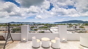 A rooftop terrace with white outdoor furniture and a view of the city and mountains. - Phuket Five Fortune Holiday Hotel (Rawai)