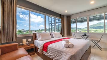 A hotel room with a large bed, a desk, a chair, and a view of the mountains.