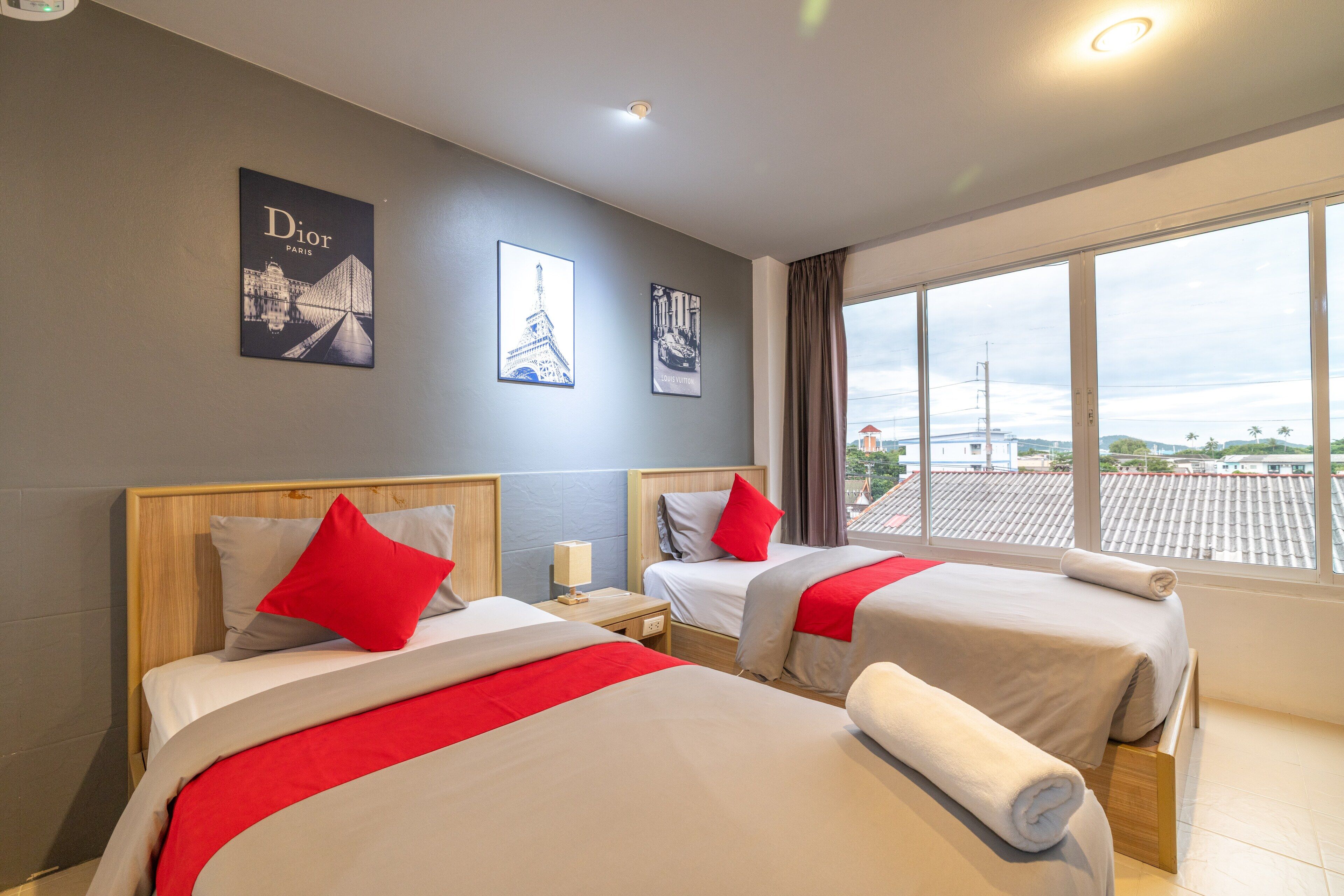 A hotel room with two beds, a nightstand, a lamp, and a window with a view of the city.