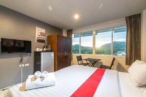Habitación de hotel con cama, escritorio, silla, televisor, armario y ventana con vista al exterior.