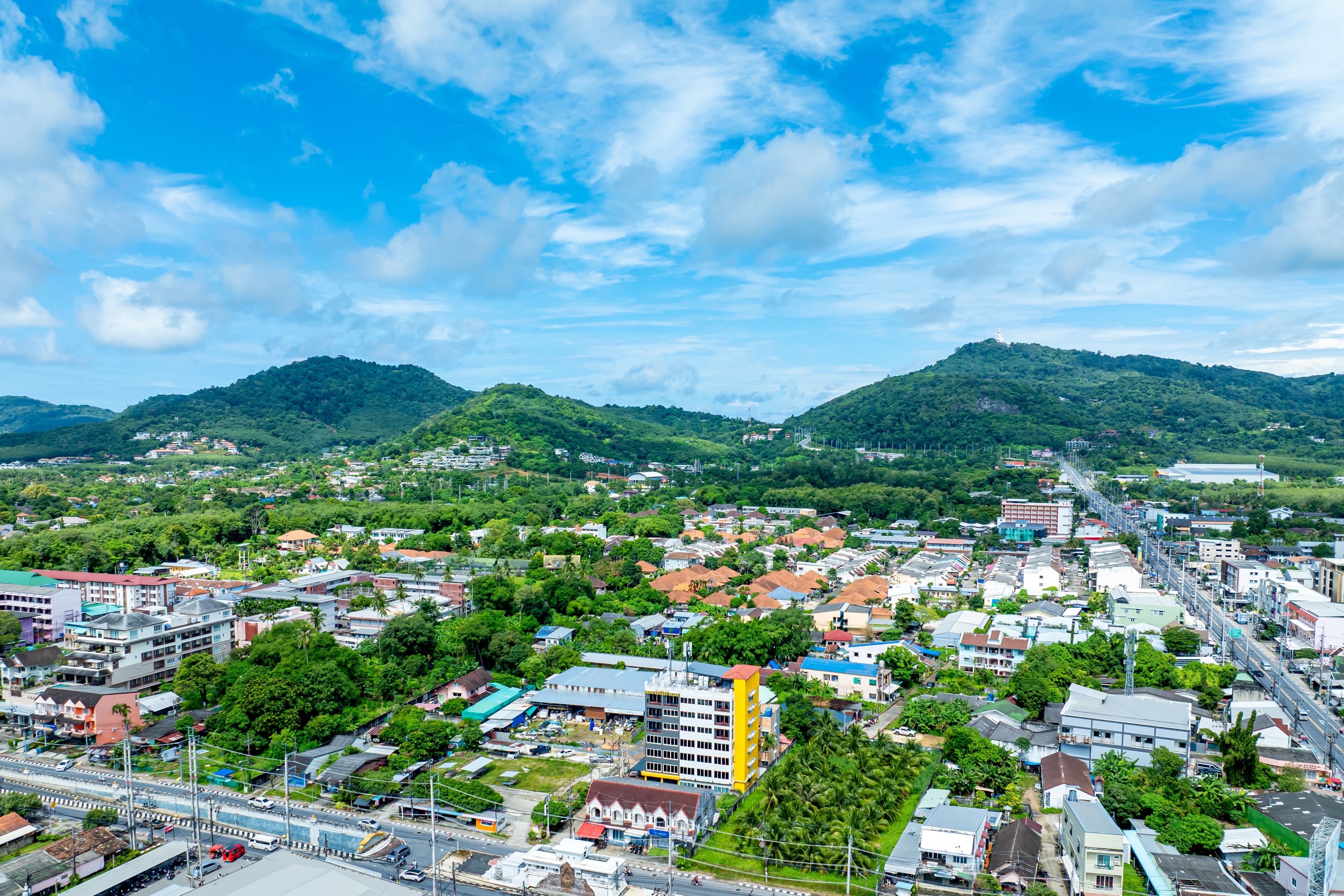 A cityscape with a prominent yellow building, surrounded by lush green hills and a clear blue sky.