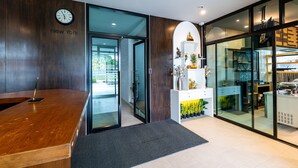 A reception area with a wooden desk, a clock displaying 'New York', and a glass door leading to a modern kitchen. - Phuket Five Fortune Holiday Hotel (Rawai)