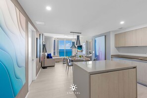 A modern kitchen with a central island, a dining area with a view, and a living space with a sofa and a TV.