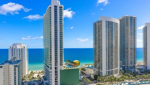 A high-rise hotel with a view of the ocean, a parking lot, and a curved road.