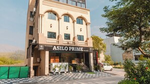 Et hotel kaldet 'ASILO PRIME' med en moderne facade, en balkon og en trappe, der fører til indgangen.