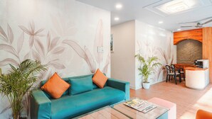 En moderne hotellobby med en turkis sofa, orange puder, et glasbord og en receptionsdisk.