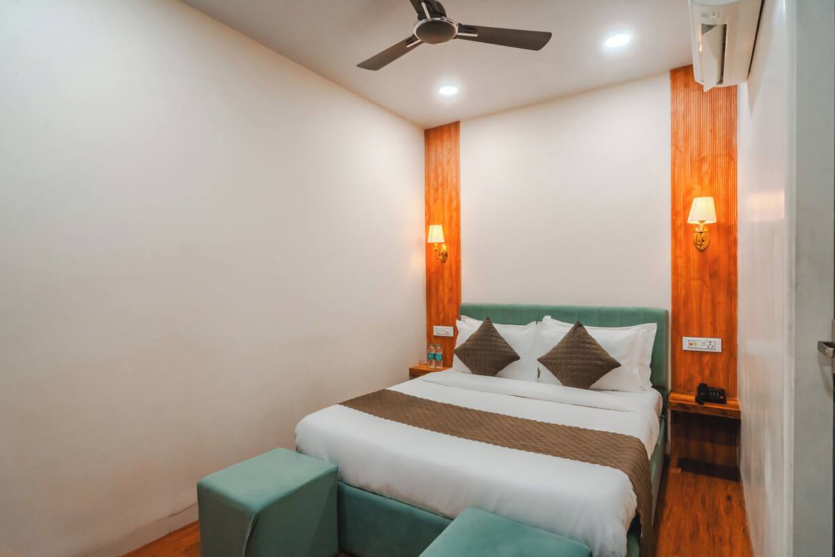 A hotel room with a bed, a ceiling fan, wall-mounted lamps, and a wooden accent wall.