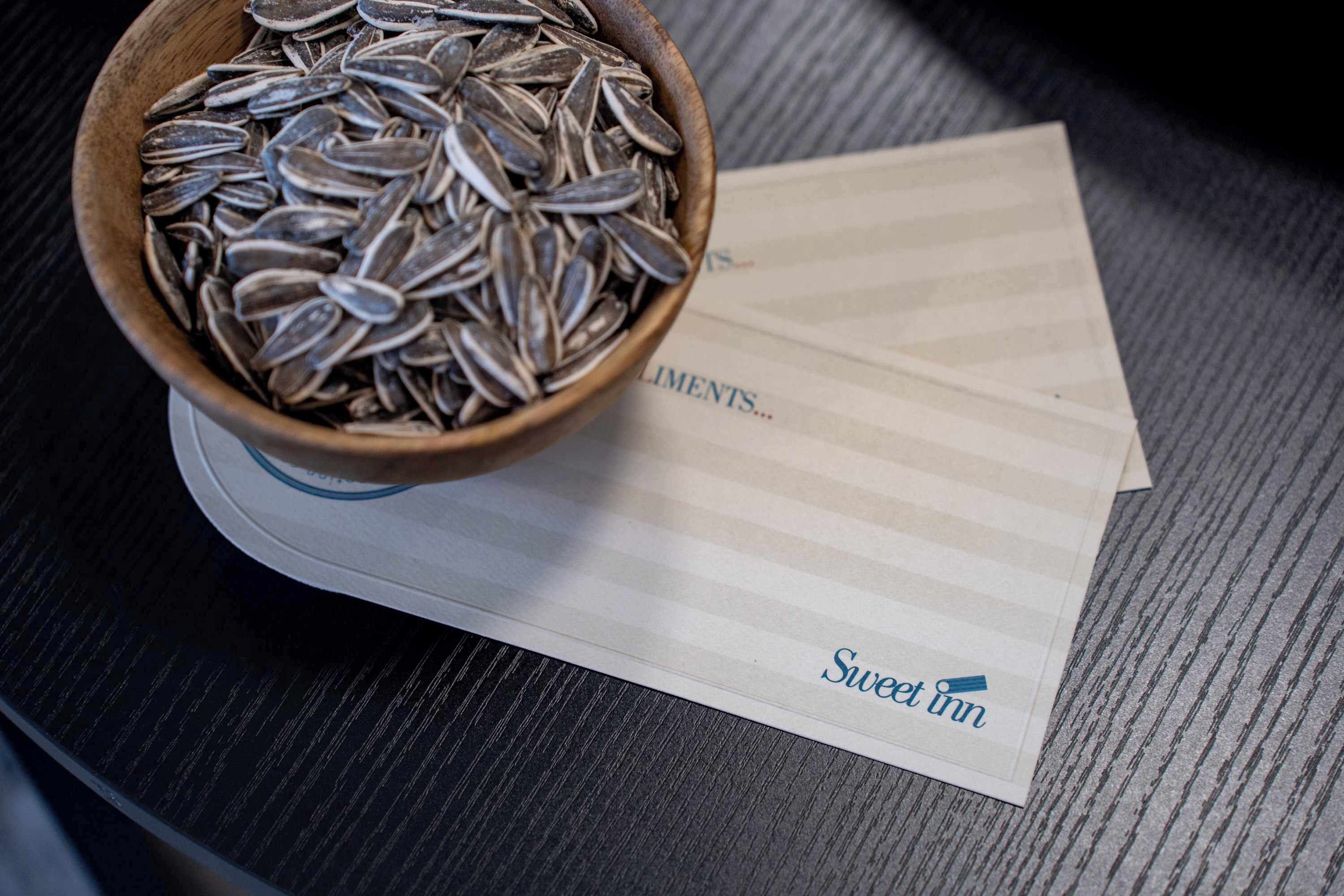 A wooden bowl filled with sunflower seeds placed on a coaster next to a notepad with the text "Sweet Inn" visible.