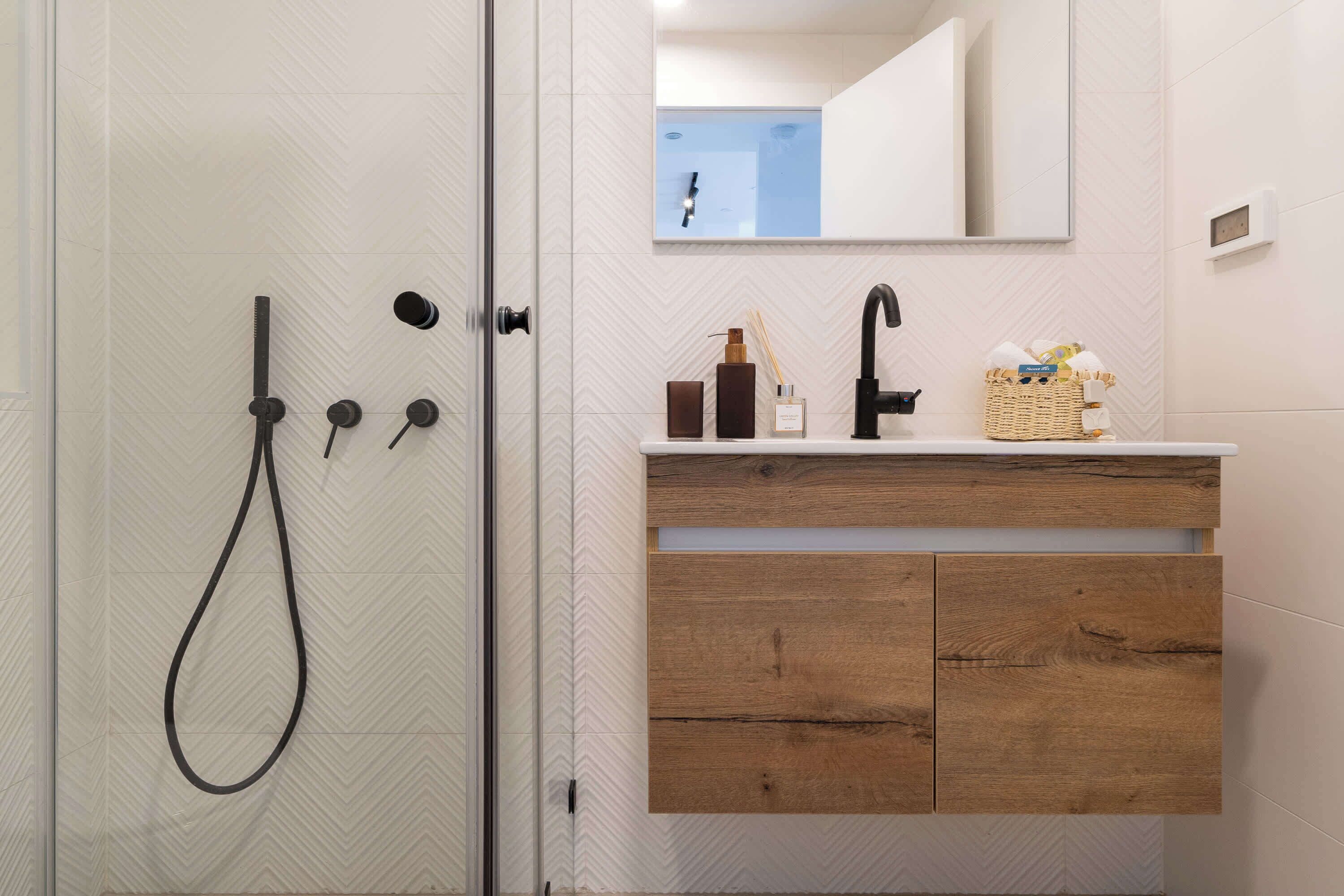A bathroom with a glass shower door, a wooden vanity with a mirror, and a sink.
