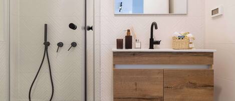 A bathroom with a glass shower door, a wooden vanity with a mirror, and a sink.