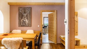 A dining area with a wooden table, chairs with fur throw pillows, a painting of a deer, and a view into another room through a doorway. - Apartment 'Bergwild' with Mountain View, Private Terrace and Wi-Fi (Garmisch-Partenkirchen)