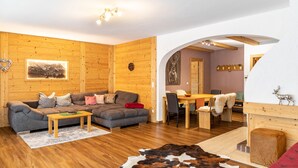 A cozy room with a wooden floor, a sofa, a dining table, and a fireplace. - Apartment 'Bergwild' with Mountain View, Private Terrace and Wi-Fi (Garmisch-Partenkirchen)