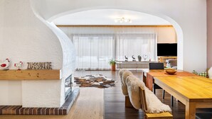 An arched living room with a fireplace, wooden beams, a dining table, and a television. - Apartment 'Bergwild' with Mountain View, Private Terrace and Wi-Fi (Garmisch-Partenkirchen)