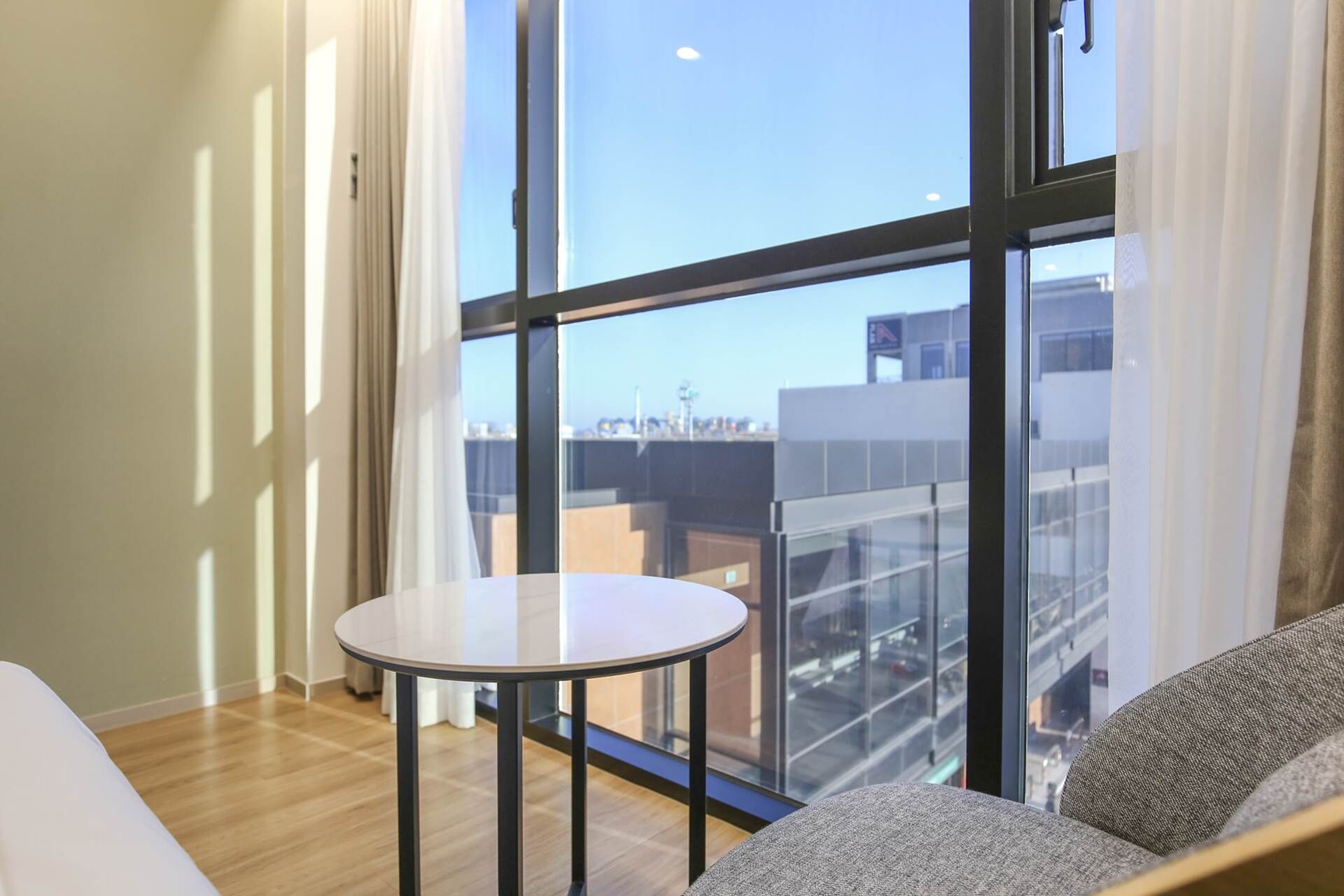 A modern living room with a round table, a sofa, and large windows offering a city view.
