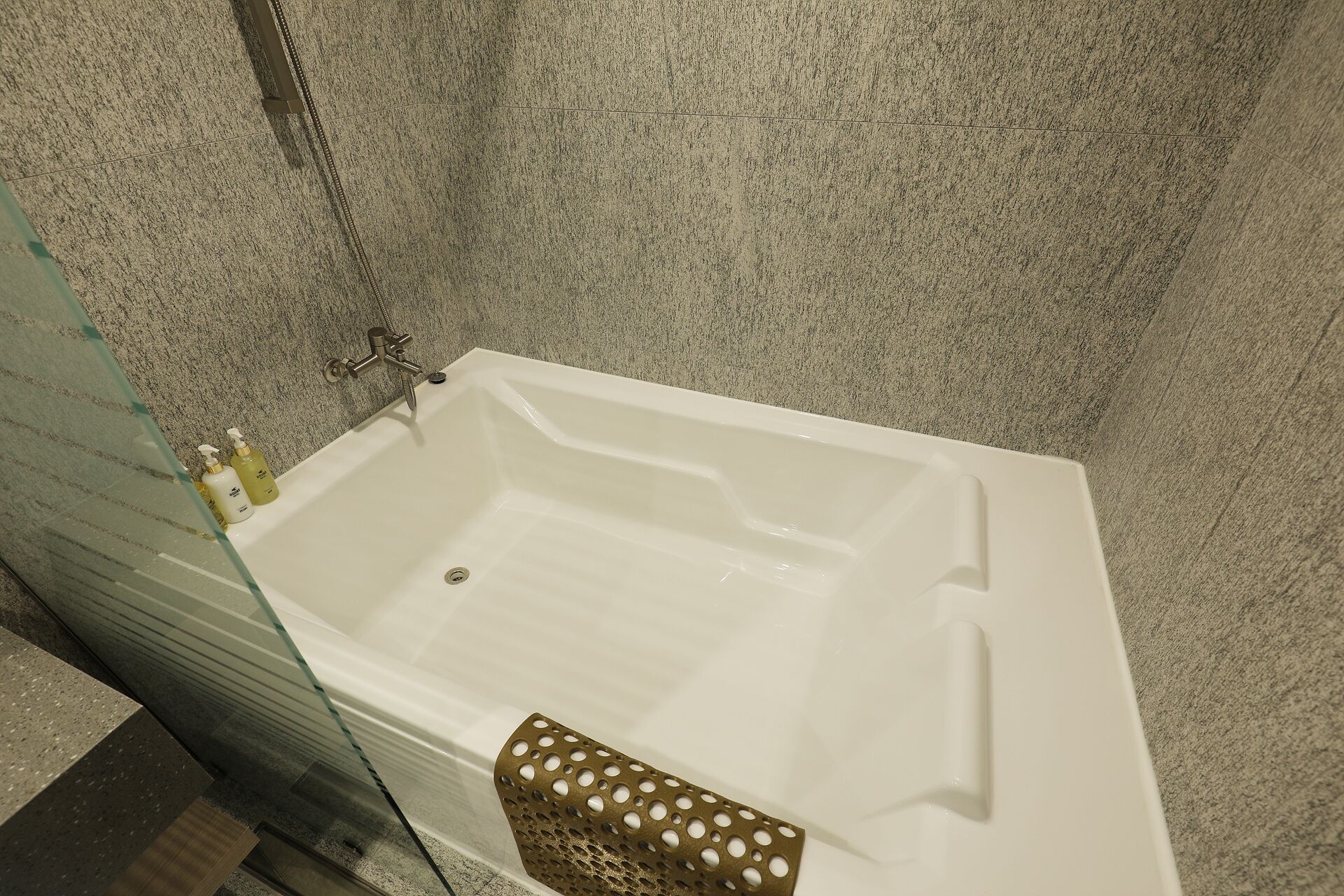 Une baignoire blanche dans une salle de bain dont le mur est texturé.
