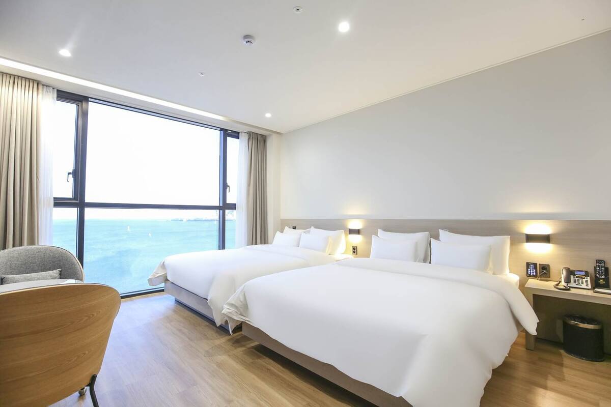 A hotel room with two beds, a chair, a nightstand, and a view of the sea.