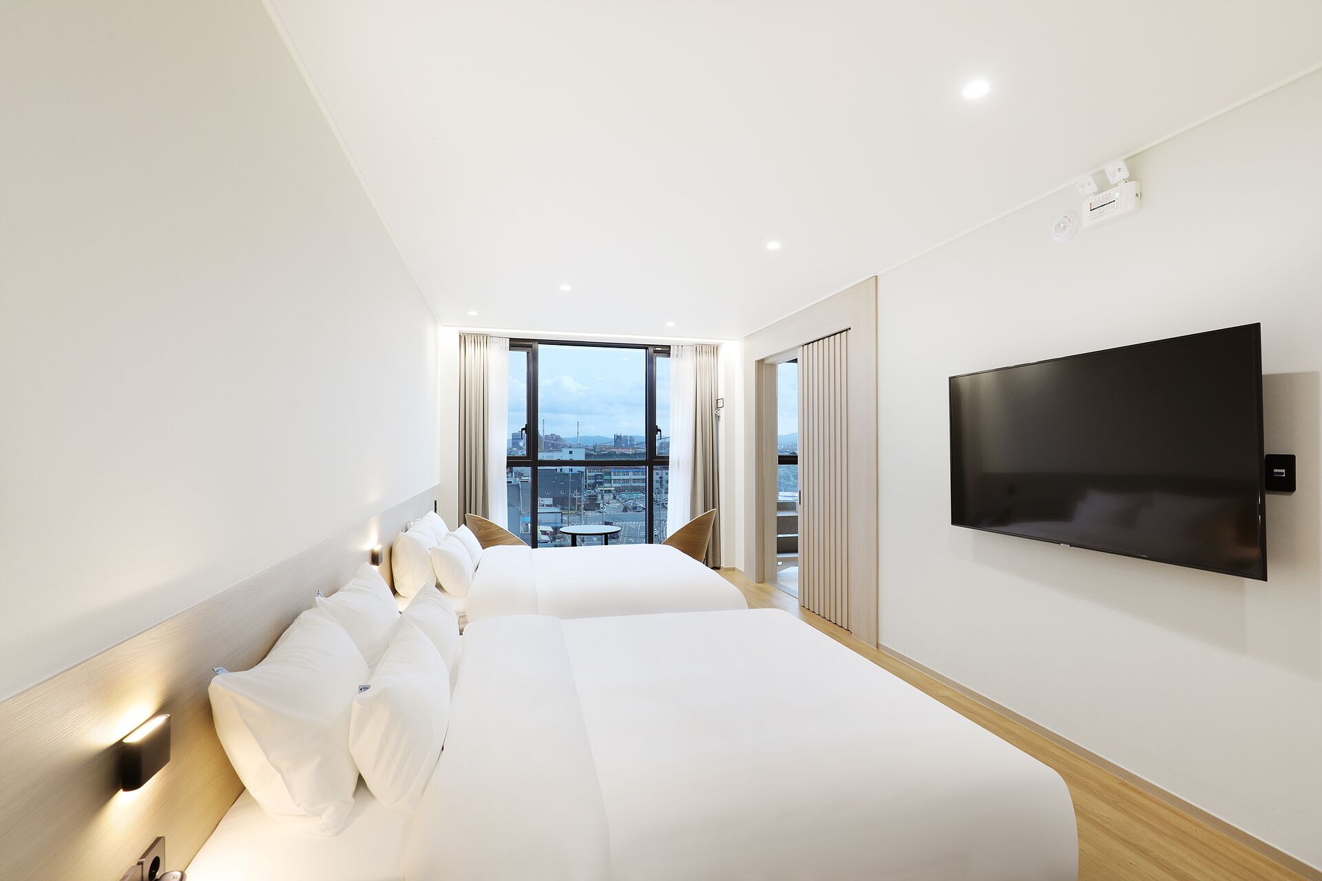 A hotel room with two beds, a TV, and a city view.