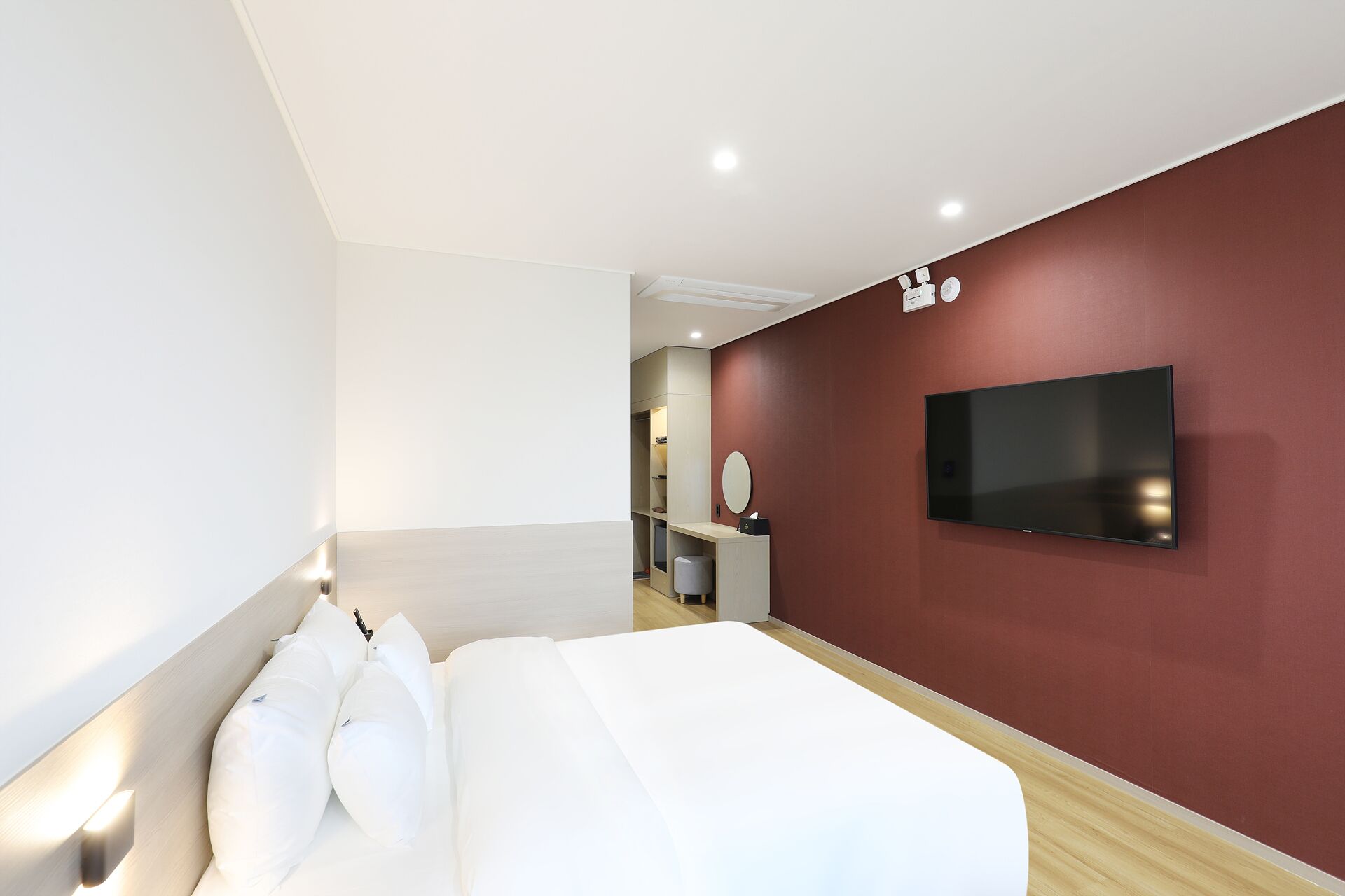 A modern hotel room with a large bed, a TV mounted on the wall, and a vanity with a mirror.