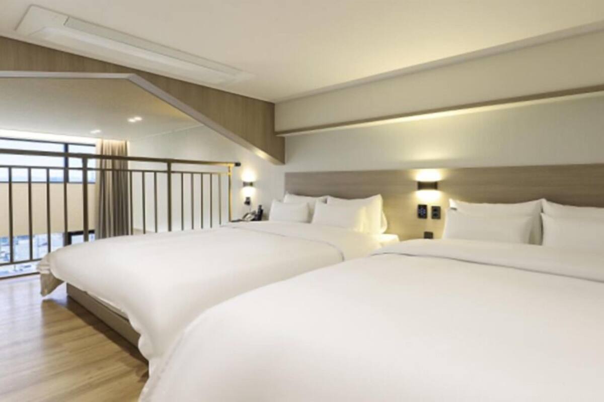 A hotel room with two large beds, a wooden floor, and a balcony with a railing.