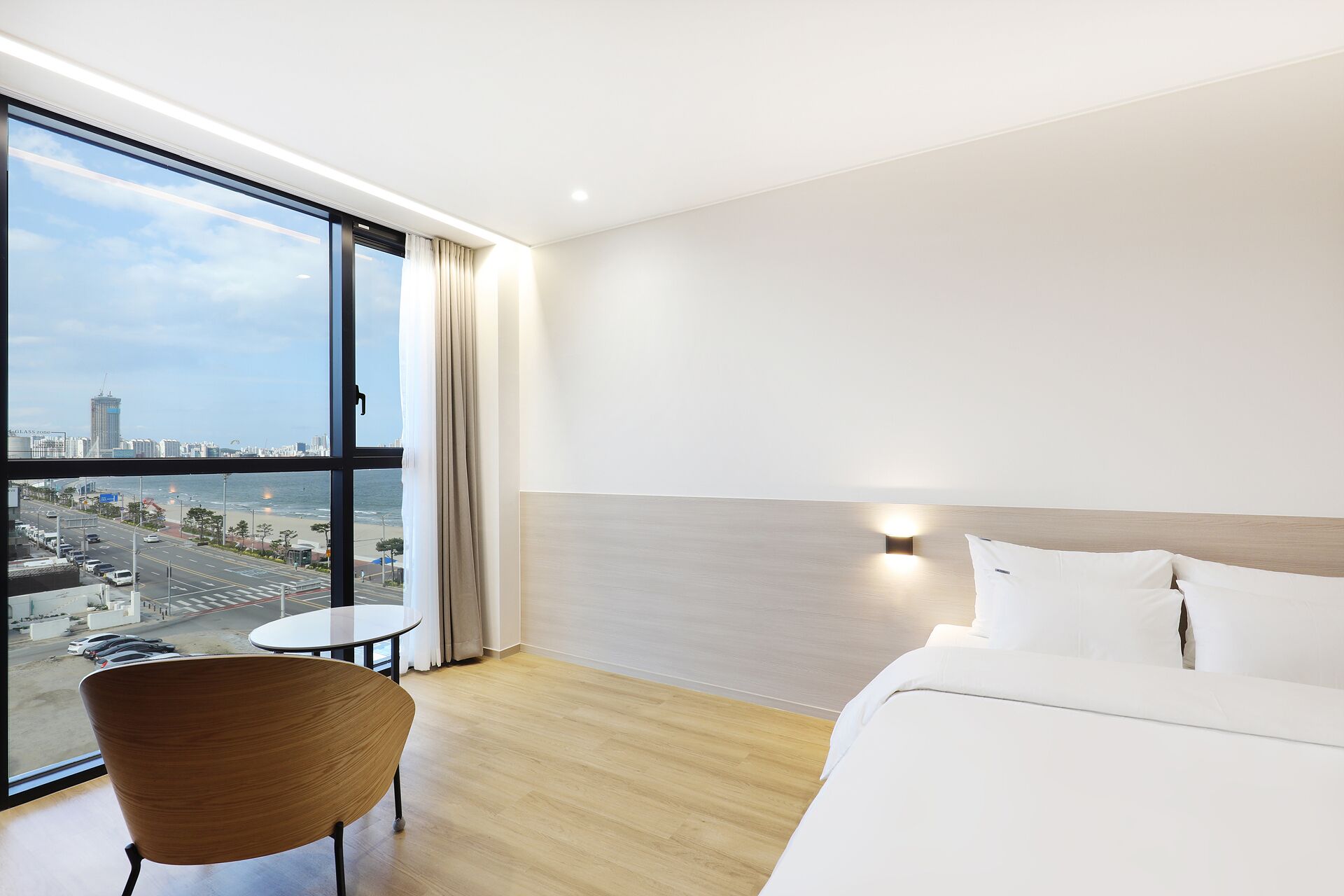 A hotel room with a large window, a bed, a chair, and a small table.
